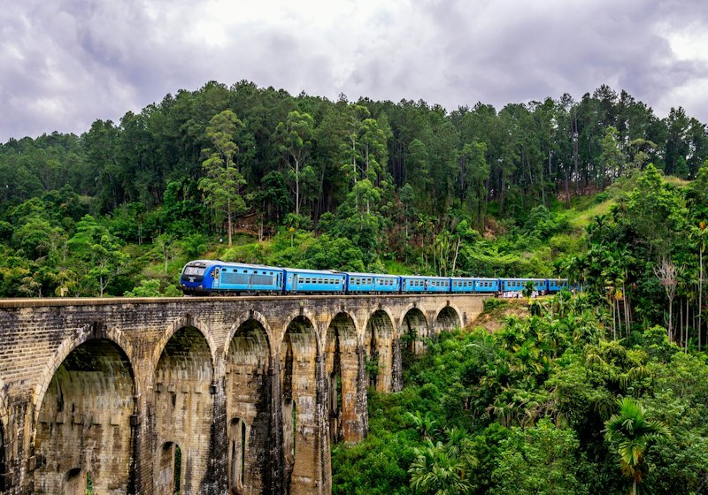 A train crossing a stone viaduct through green hill country